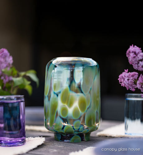 canopy glass house, hand-blown glass hurricane with glassybaby in it one wood table at night.