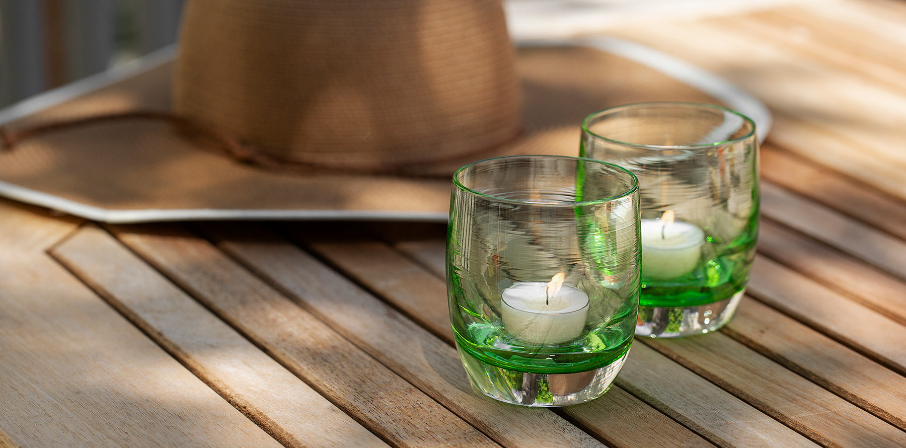 a beautiful bright green transparent hand-blown glass candle holder. sitting on a wood table in the sunshine, named clover.