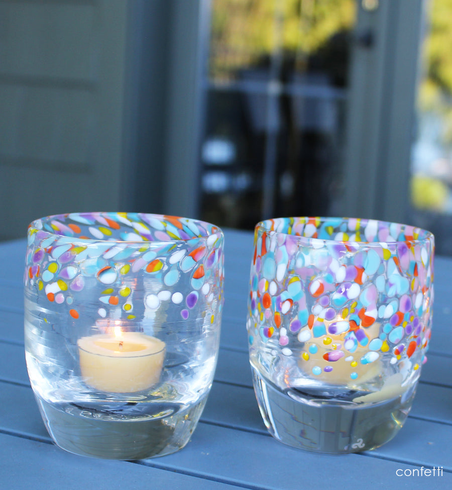 Two colorful glass candle holders with candles on a blue surface outdoors.
