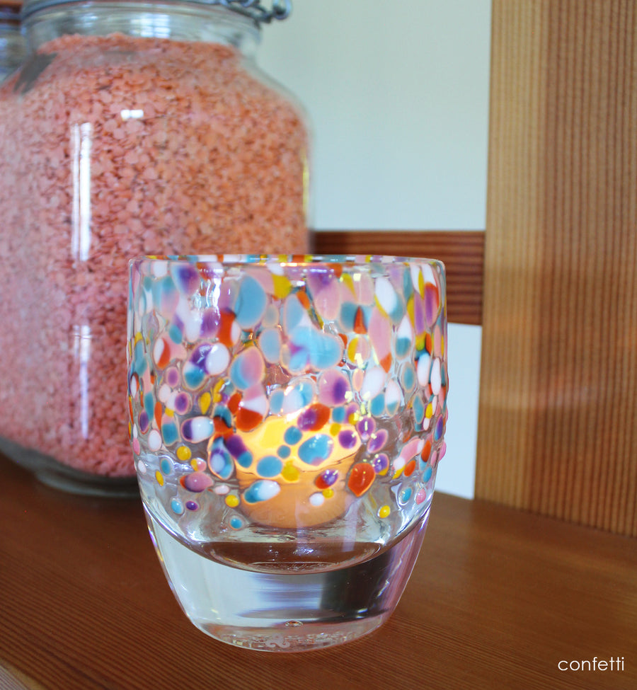 Colorful glass candle holder with a lit candle on a wood shelf