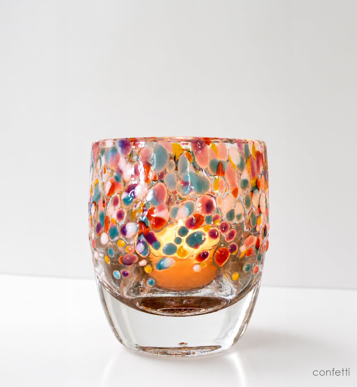Colorful glass candle holder with a lit candle on a white background