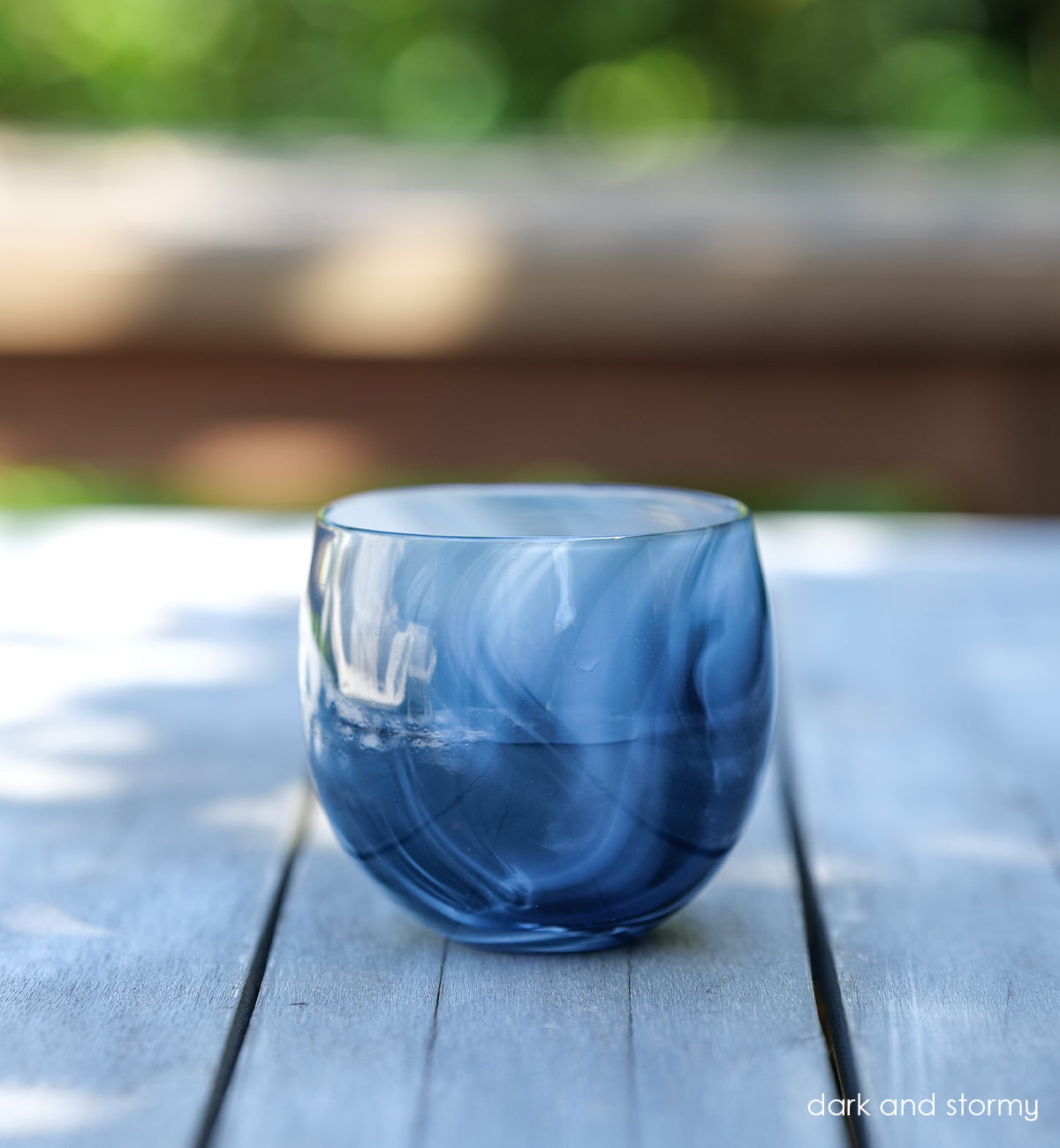 dark and stormy deep blue and white swirled hand-blown drinking glass with liquid inside on a patio table.