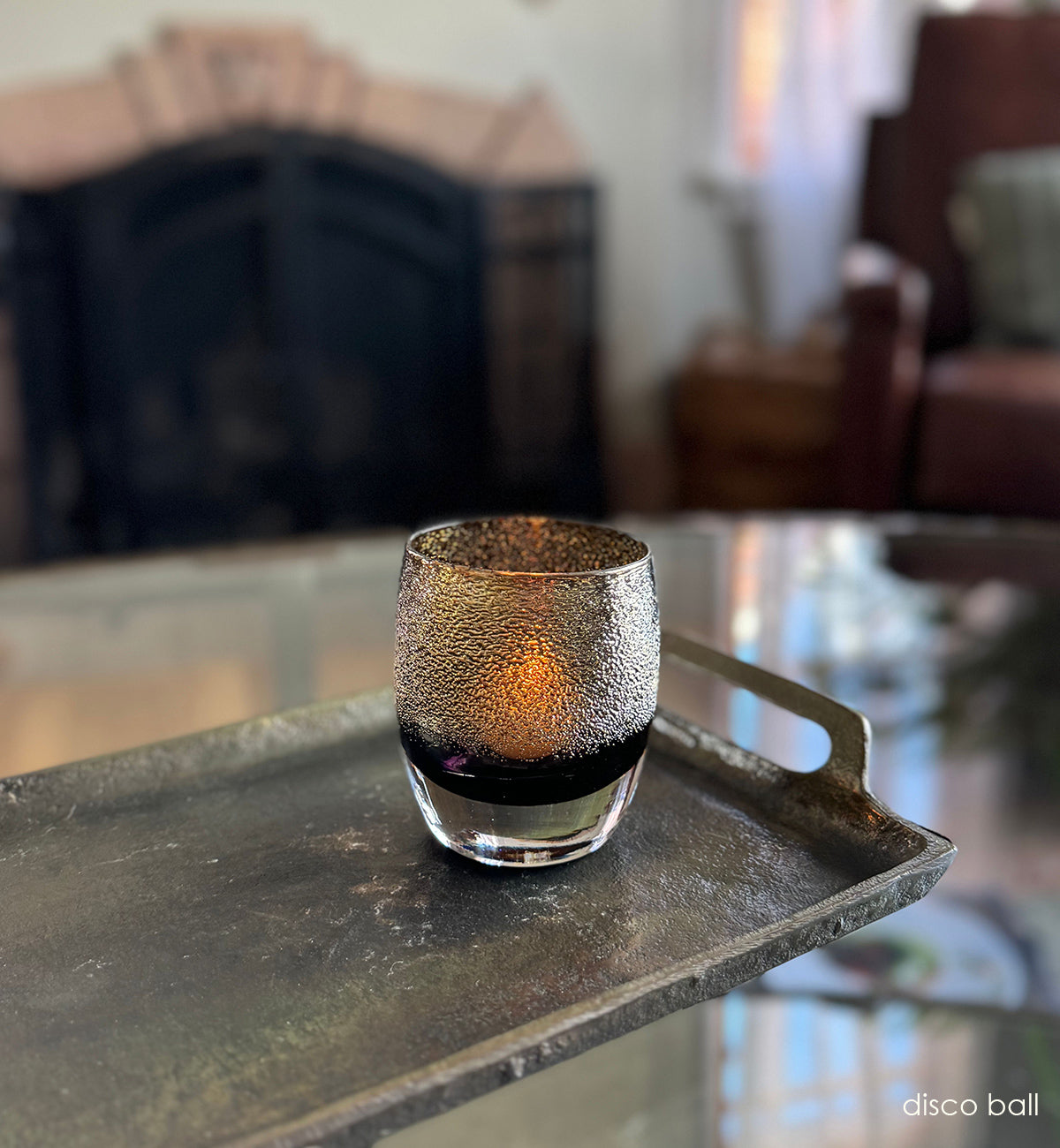disco ball, black and gold shimmer hand-blown glass votive candle holder on a metal tray on a clear glass coffee table in a living room.