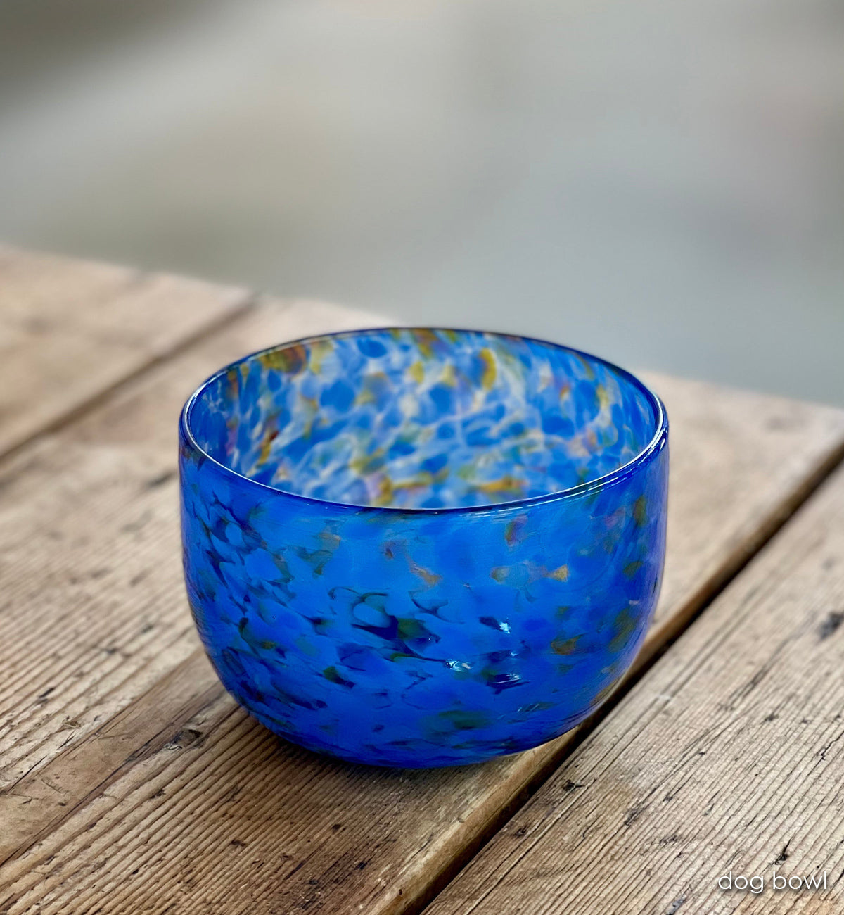 Blue glass dog bowl with speckled pattern on a wooden surface
