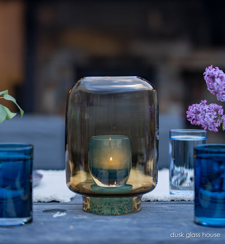 dusk glass house, hand-blown glass hurricane with glassybaby in it one wood table at night.