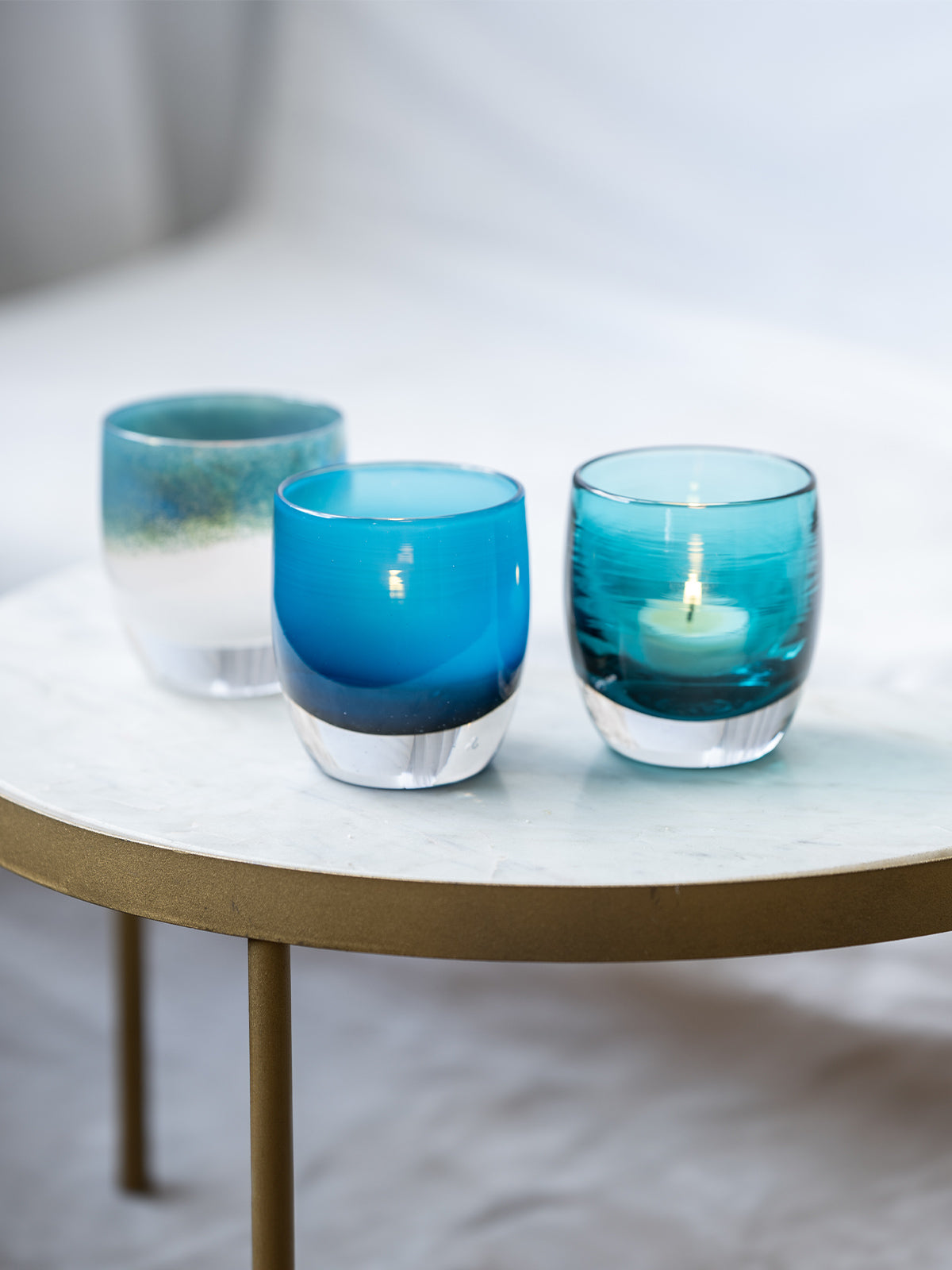 Three blue glass candle holders with candles on a white surface.
