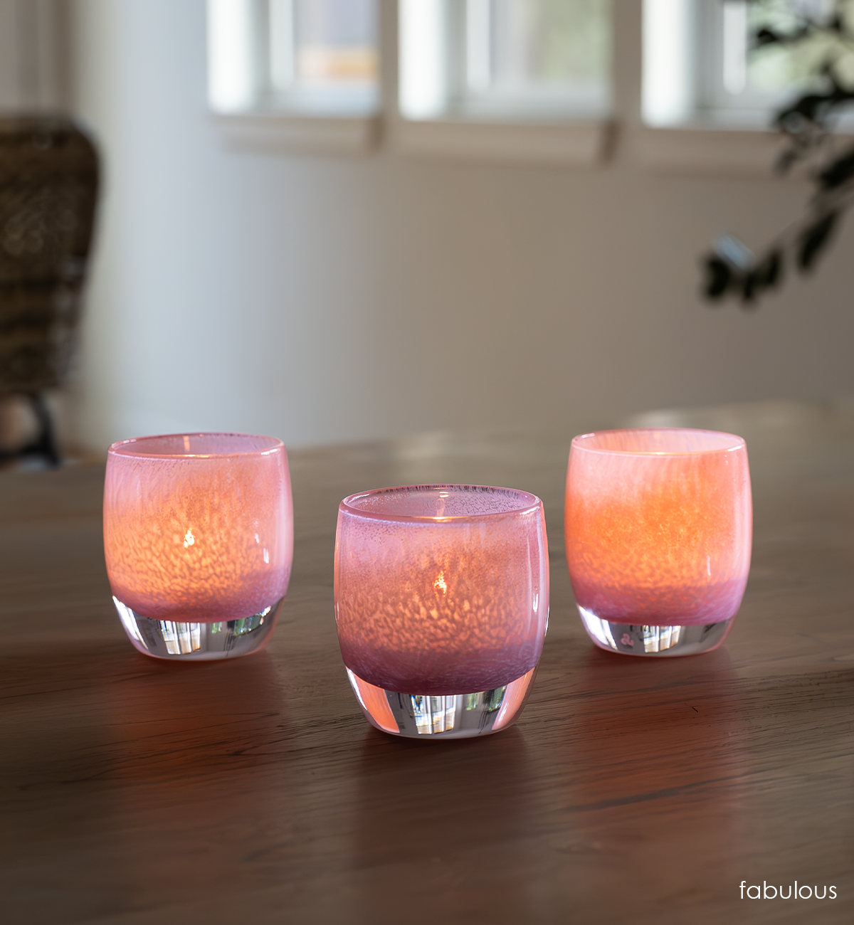 three fabulous, pink textured hand-blown glass votive candle holders on a wood dining room table.