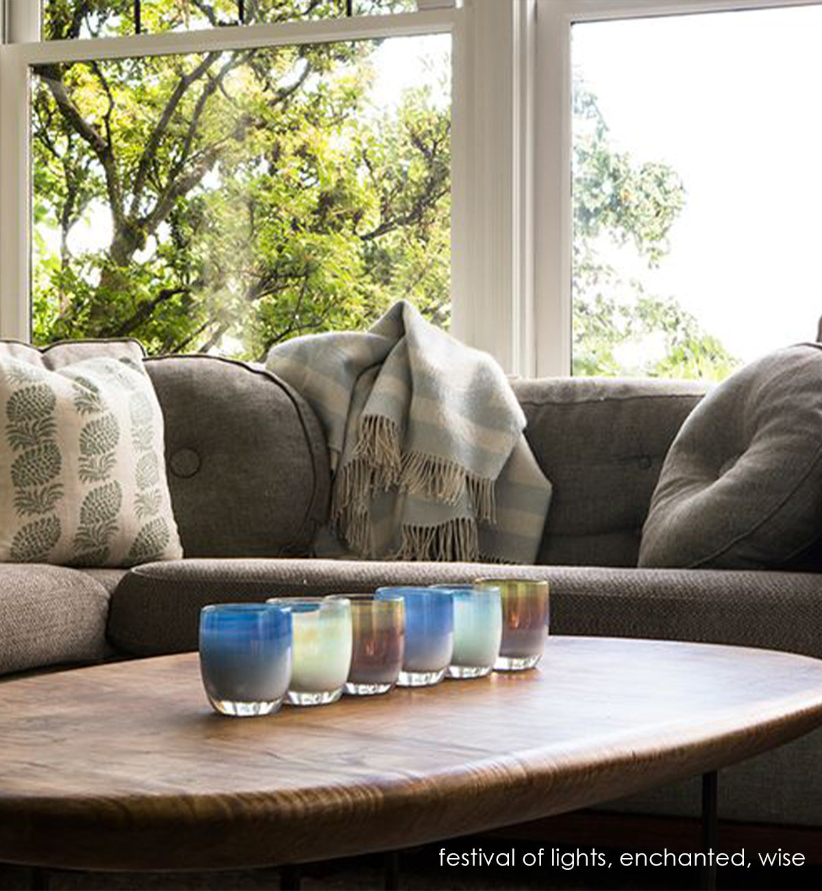 festival of lights, light and dark blue with metallic luster hand-blown glass votive candle holder with wise and enchanted on a wood coffee table next to a gray couch.