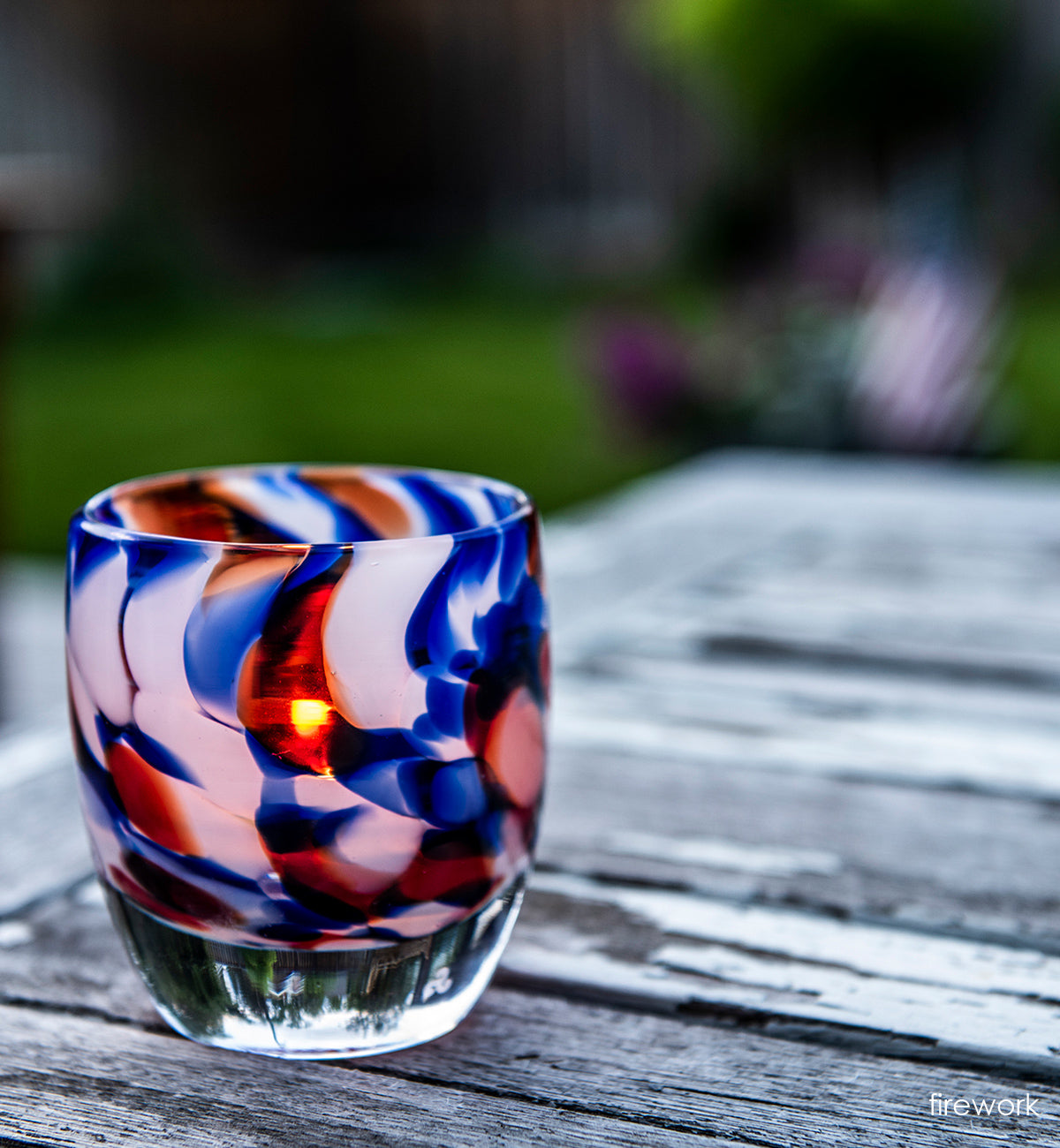 firework, red white and blue petal, hand-blown glass votive candle holder on a wood patio table.