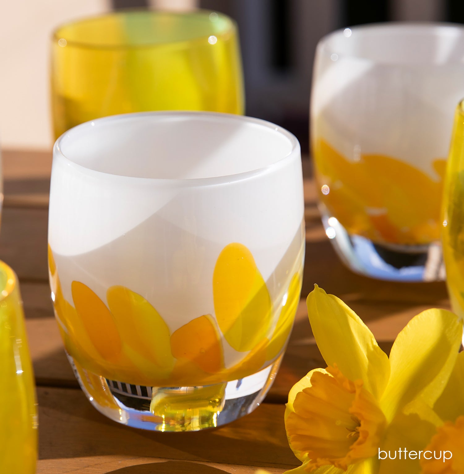 buttercup, yellow petals on white, hand-blown glass votive candle holders on a wood table with fresh daffodil flowers.