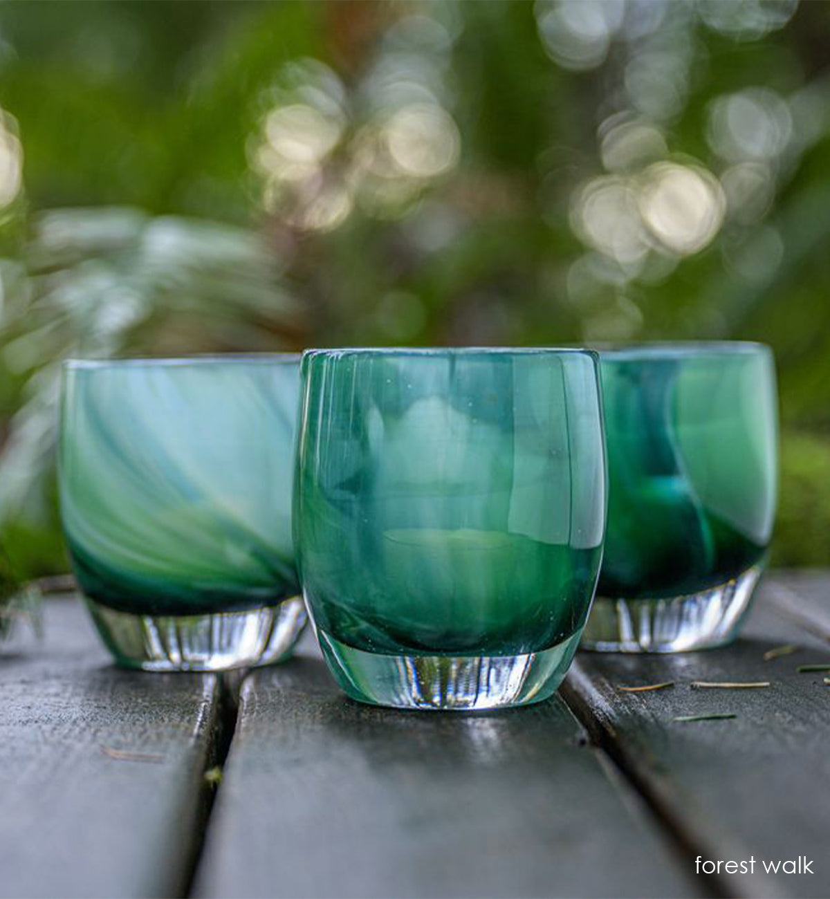 three forest walk, translucent green swirl hand-blown glass votive candle holders sitting on wood picnic table outside.