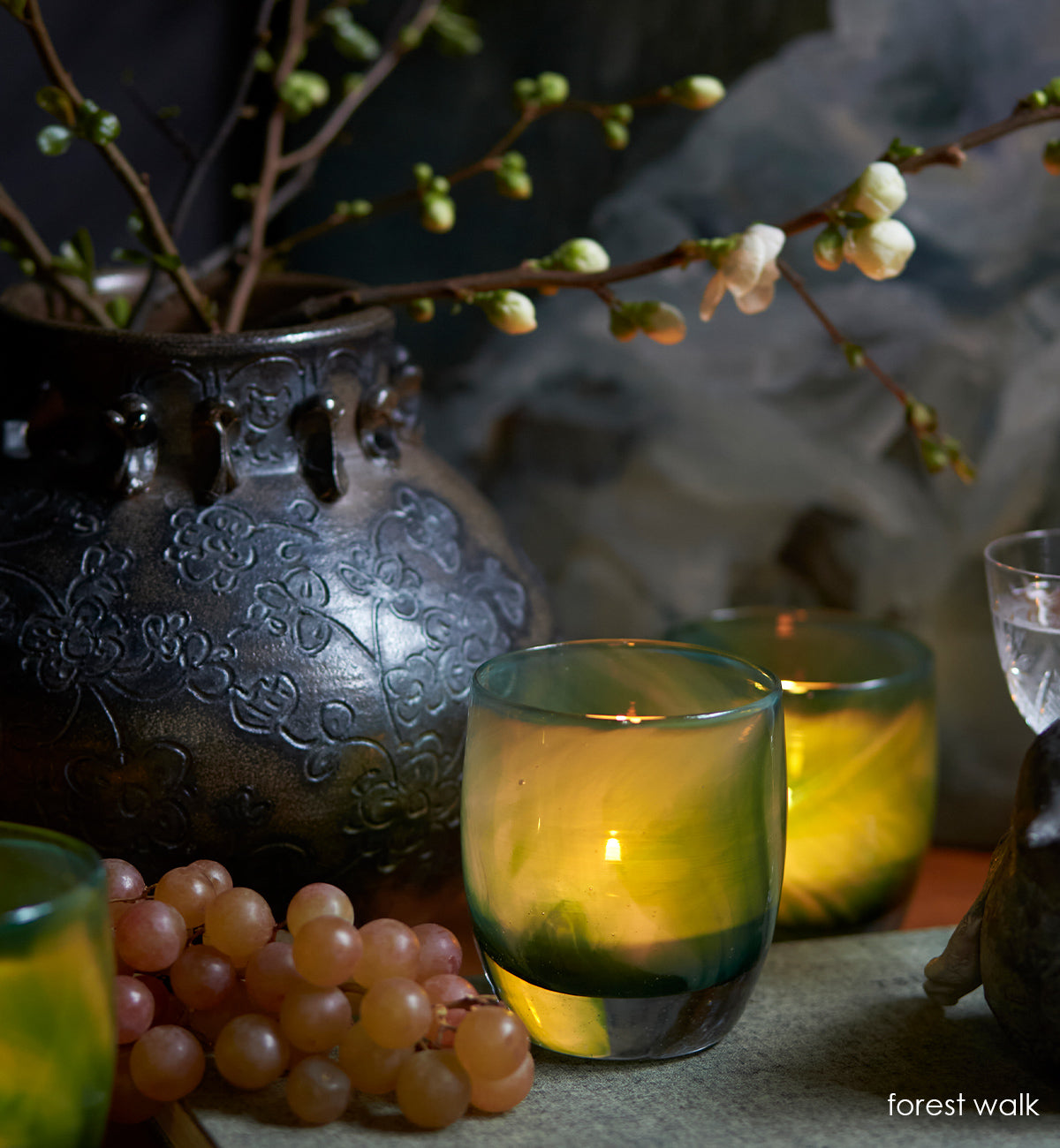 forest walk, translucent green swirl hand-blown glass votive candle holder in a still life setting with grapes and vase.