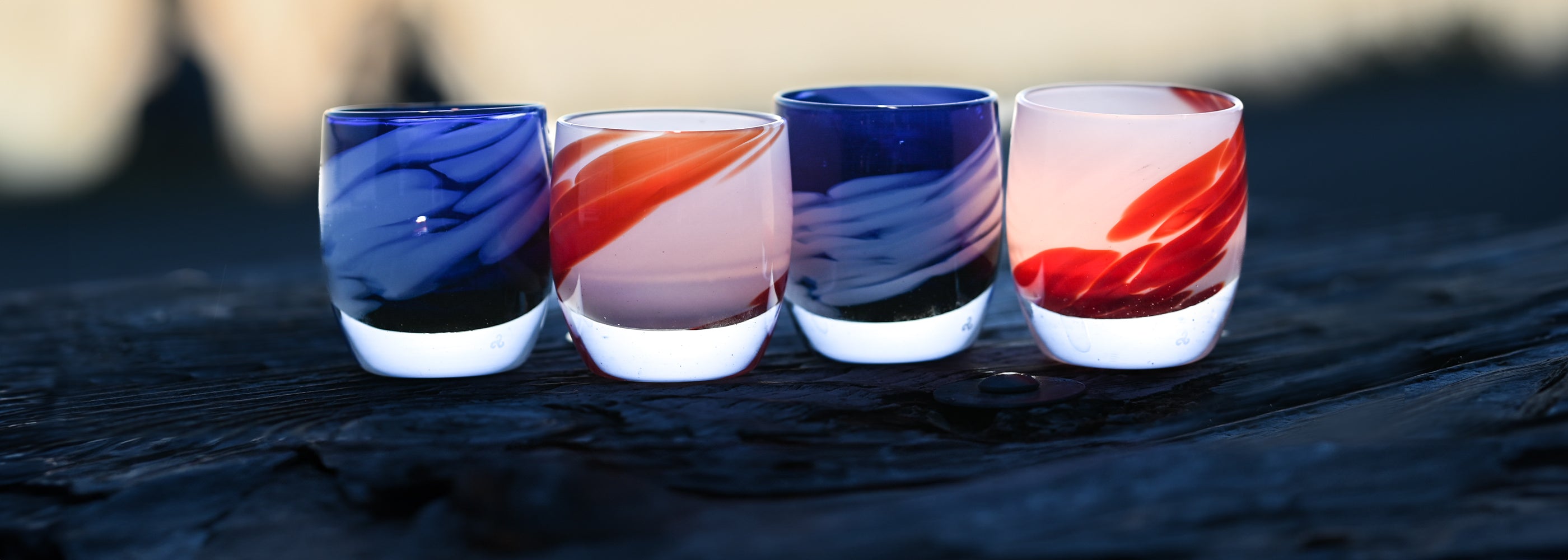 red white and blue glassybaby sitting on wood rail by a lake at sunset