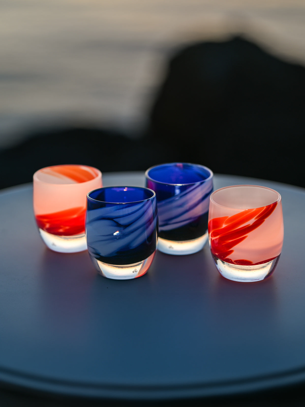 red white and blue glassybaby sitting on table by a lake at sunset