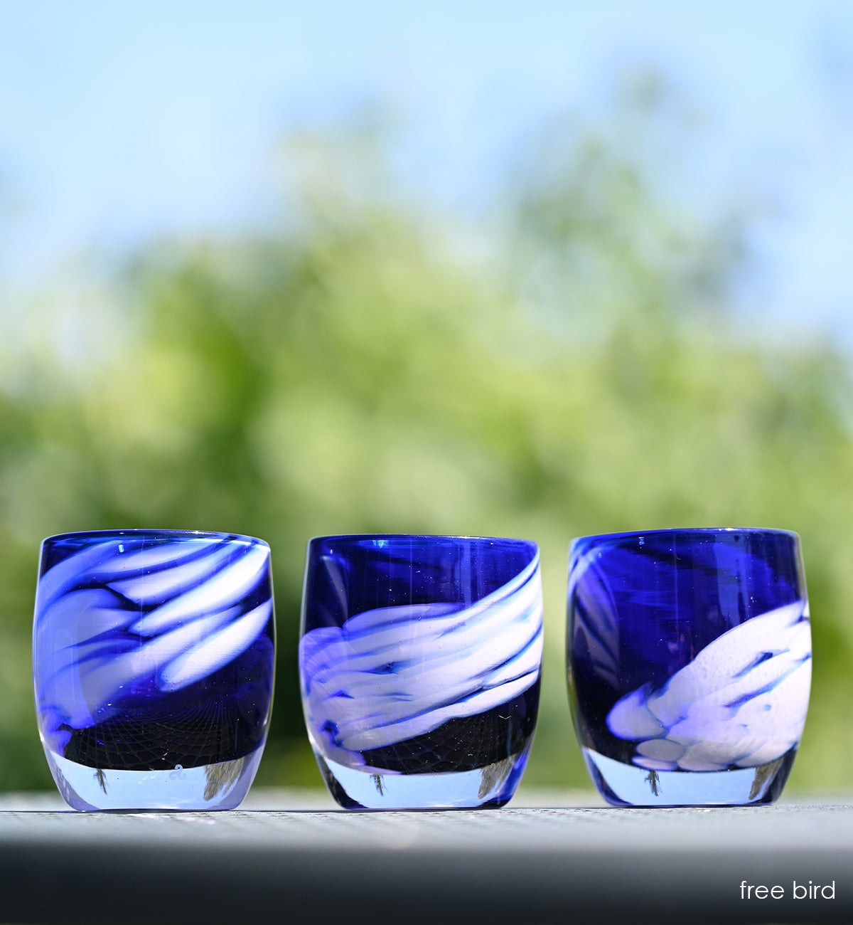 three freebird blue with white wing, hand-blown glass votive candle holders sitting side by side on an outdoor ledge.