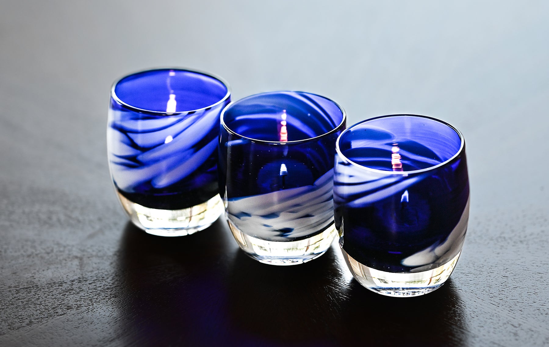 free bird is an electric blue and white patterned hand-blown glass candle holder - a set of 3 sit on a black table lit. 
