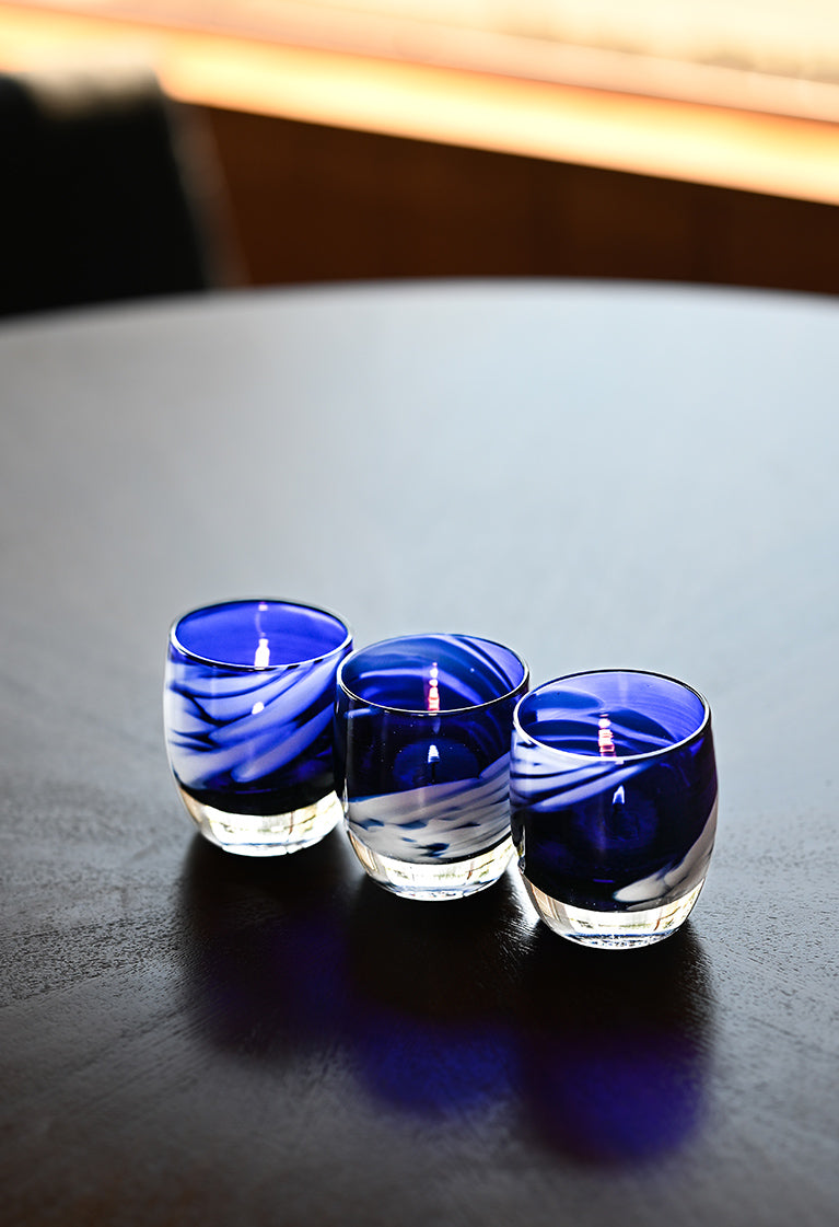 free bird is an electric blue and white patterned hand-blown glass candle holder - a set of 3 sit on a black table lit. 