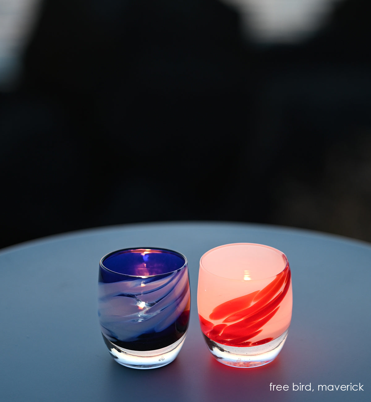 freebird blue with white wing, maverick white with red wing, hand-blown glass votive candle holders. on dim lighting on a circular table.