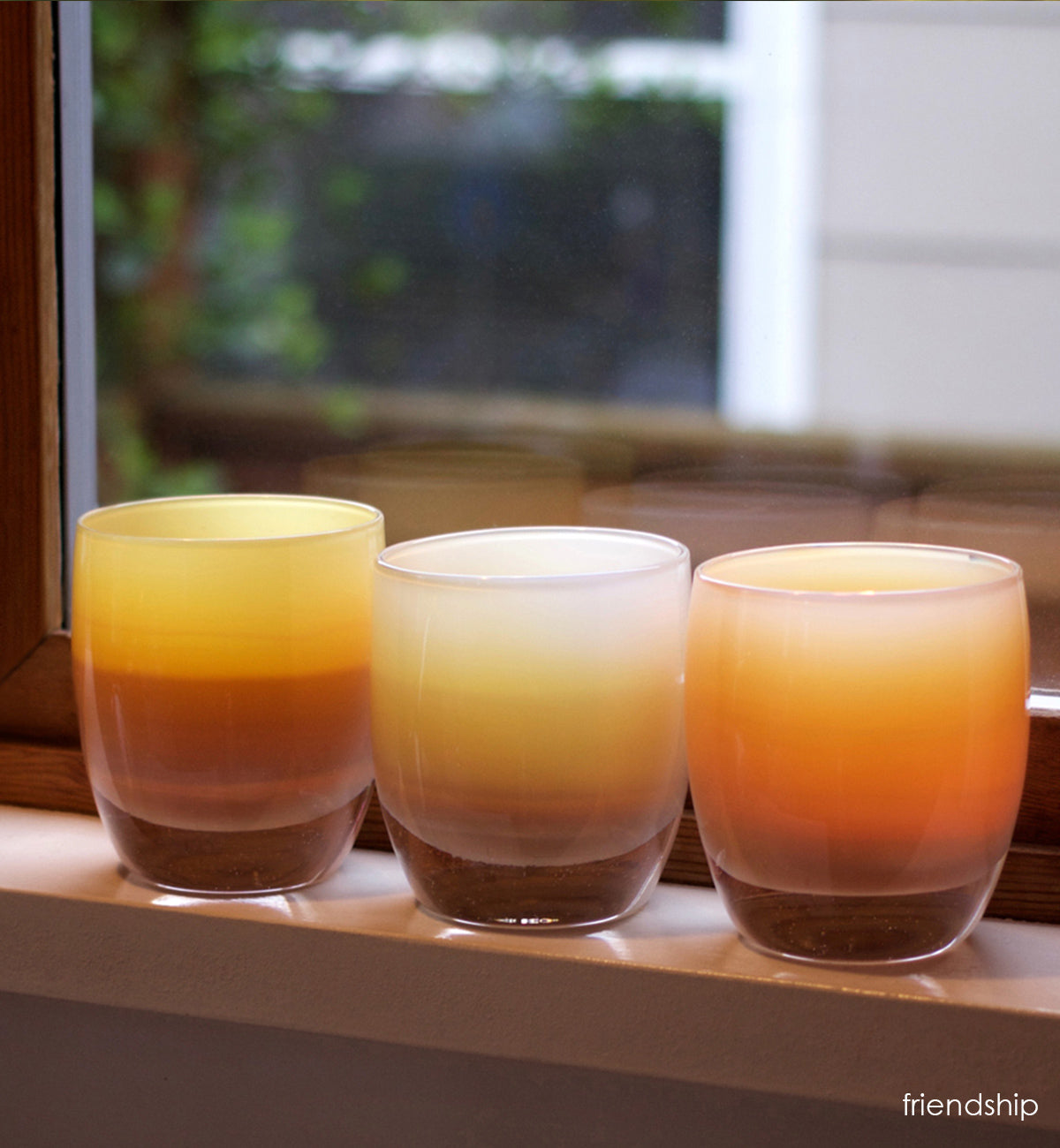 three friendship hand-blown soft yellow with brown banding glass votive candle holders perched on a windowsill.