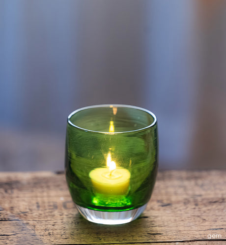 transparent green glass candle holder with a lit candle on a wooden surface