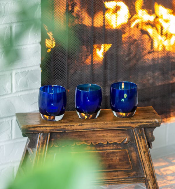 give hand-blown sapphire blue with silver metallic interior, hand-blown glass votive candle holders on a wooden stool in front of a fireplace.