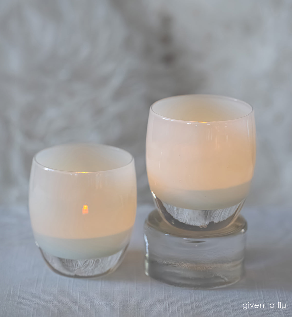 Two glass candle holders with candles on a textured surface