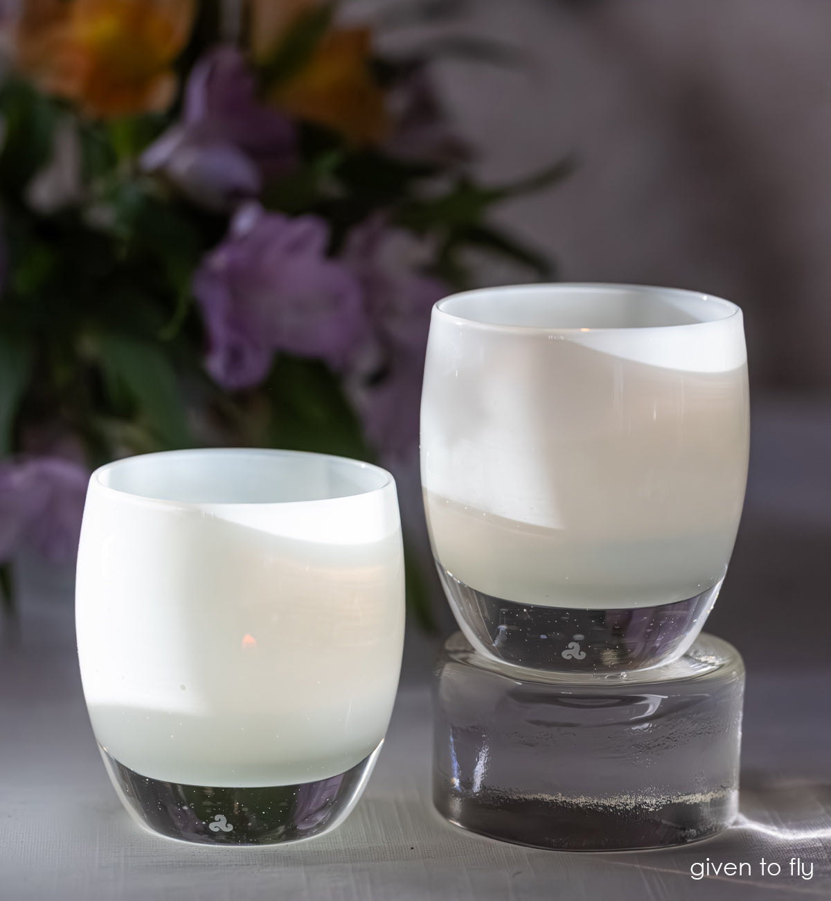Two white glass candle holders with a blurred floral background