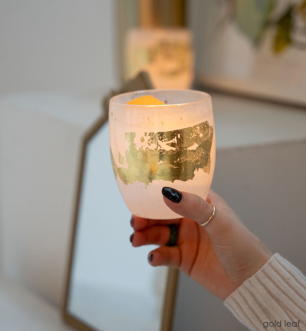 gold leaf white with 24k gold hand-blown glass votive candle holder held by a hand, with a mirror in background.