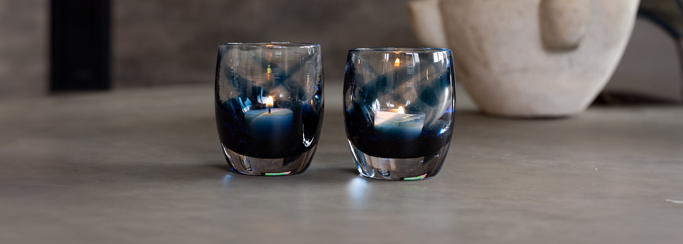 two 'good vibes' a blue and clear, hand-blown glass candle holders on gray granite table with a white bowl in the back ground 