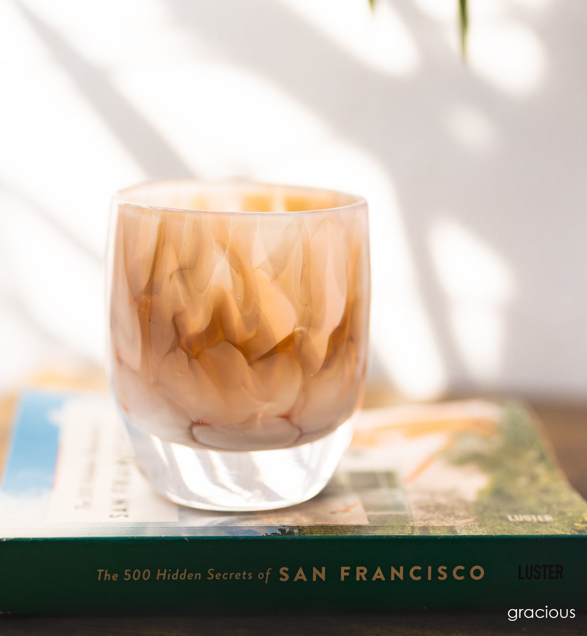 white and brown petal, hand-blown glass votive candle holder sitting on a book with green spine. white all background.