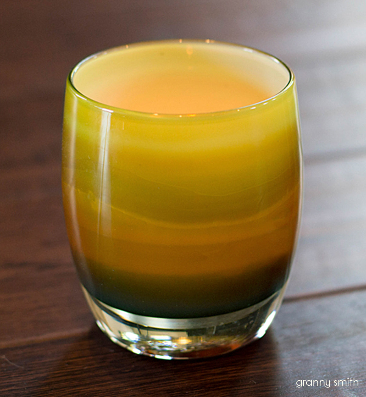 granny smith, striped green with a stark white interior, hand-blown glass votive candle holder glowing with a lit tealight inside on a wood surface.
