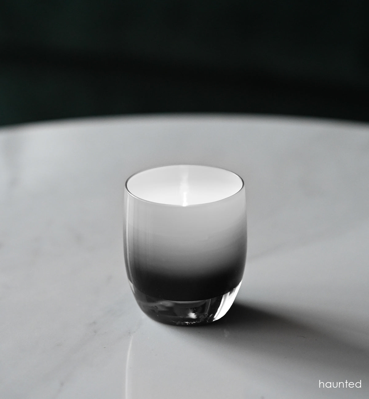 haunted black double overlay hand-blown glass votive candle holder on a marble table, lit with a tealight.