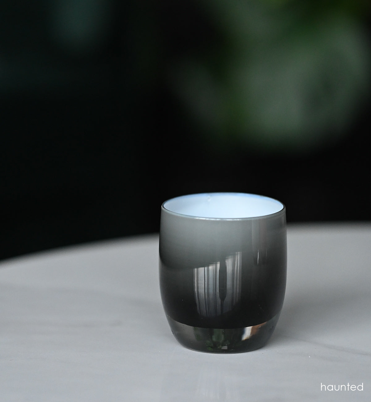 haunted black double overlay hand-blown glass votive candle holder on a marble table outside.