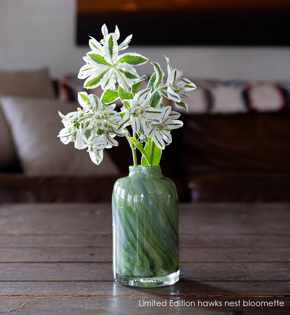 Limited Edition hawks nest bloomette vase green with blue swirls hold white flowers.