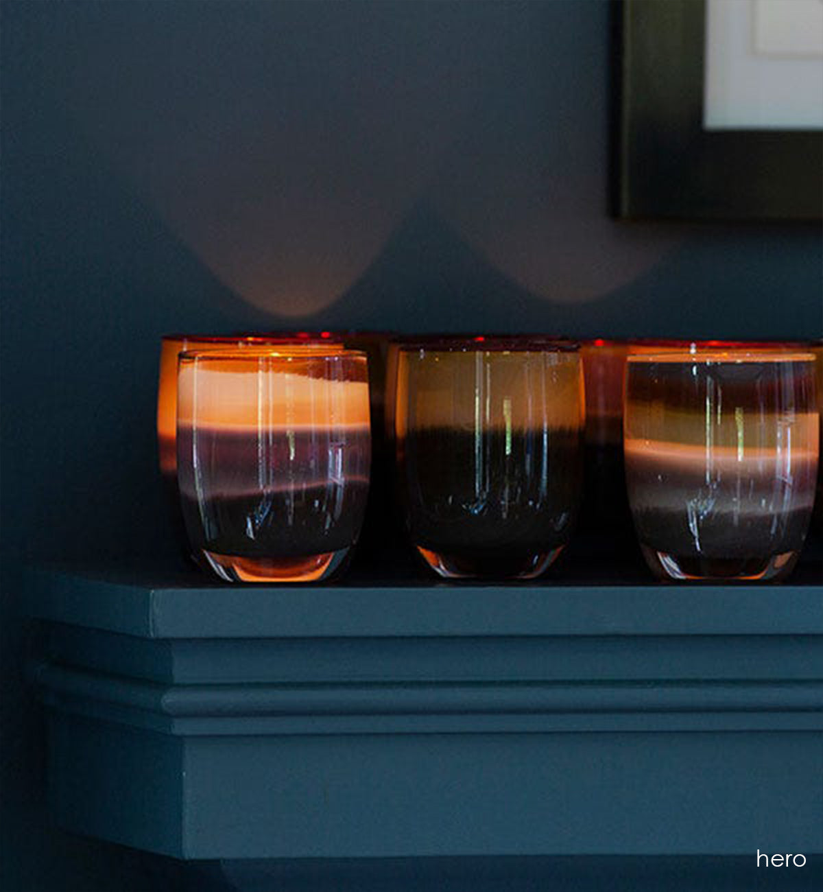 several hero multi brown hand-blown glass votive candle holders lit on a fireplace mantle.