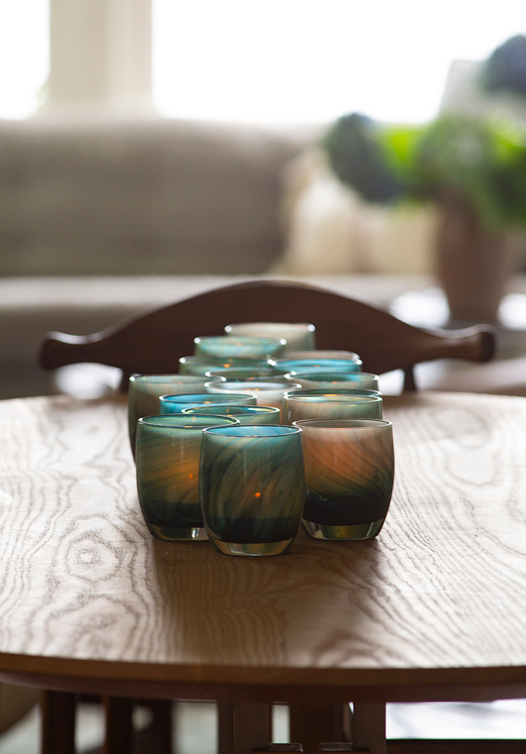 a large grouping of deep blue swirled patterned hand-blown glass candle holders sitting on a wood table.