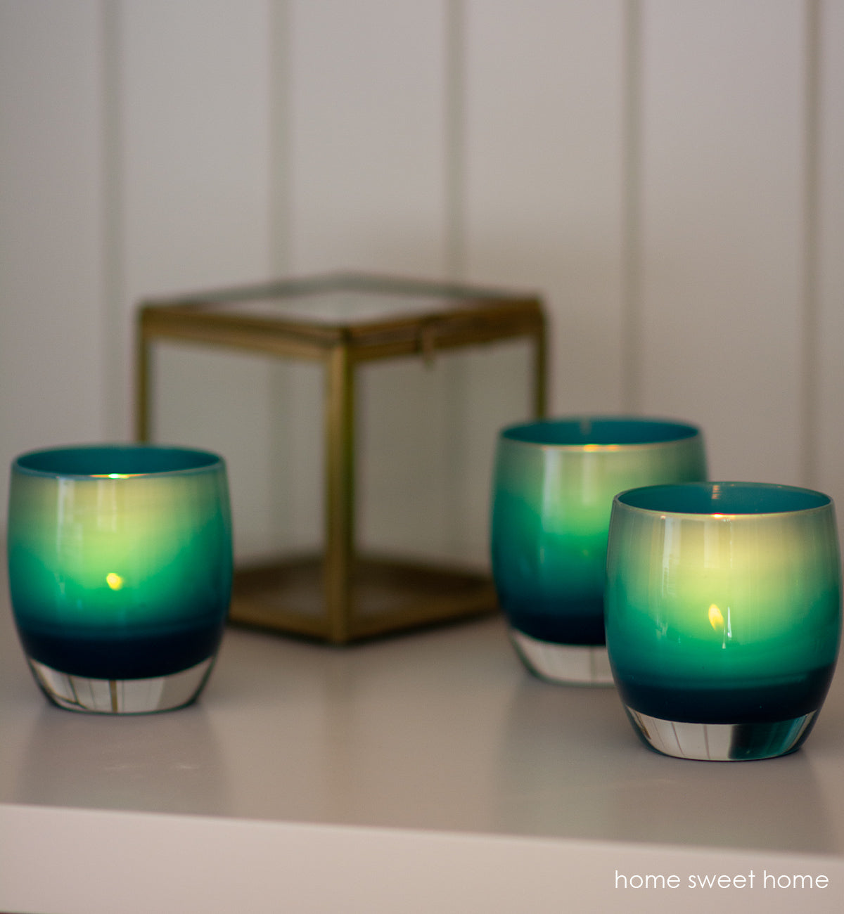 three home sweet home deep blue, hand-blown glass votive candle holders on a white mantle with a decorative box.
