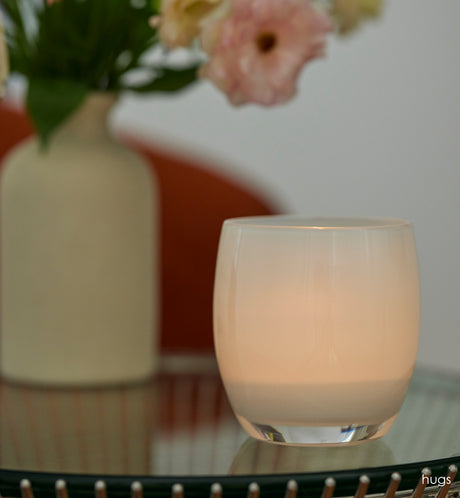 hugs opaque off white hand-blown glass votive candle holder on a table with a white ceramic vase.
