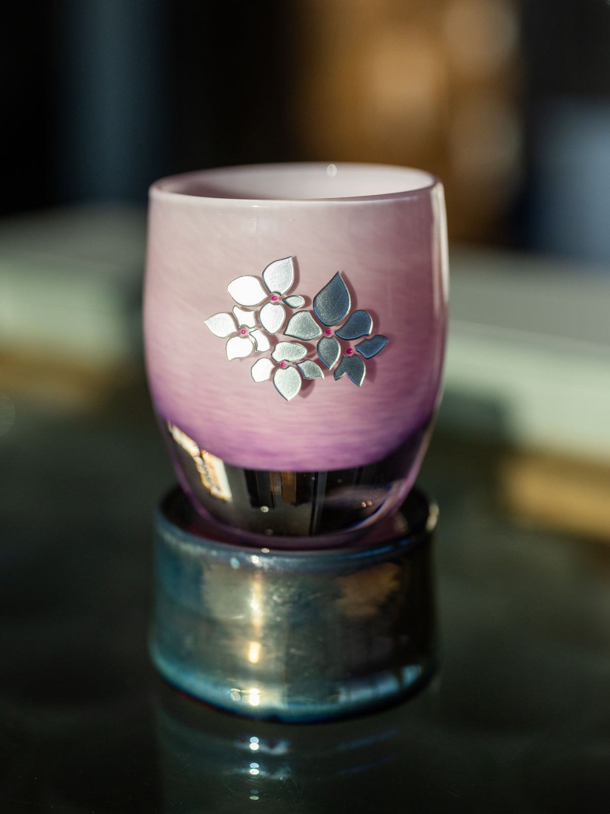 Pink glass with hand etched hydrangea design sitting on a pedestal on a dark surface
