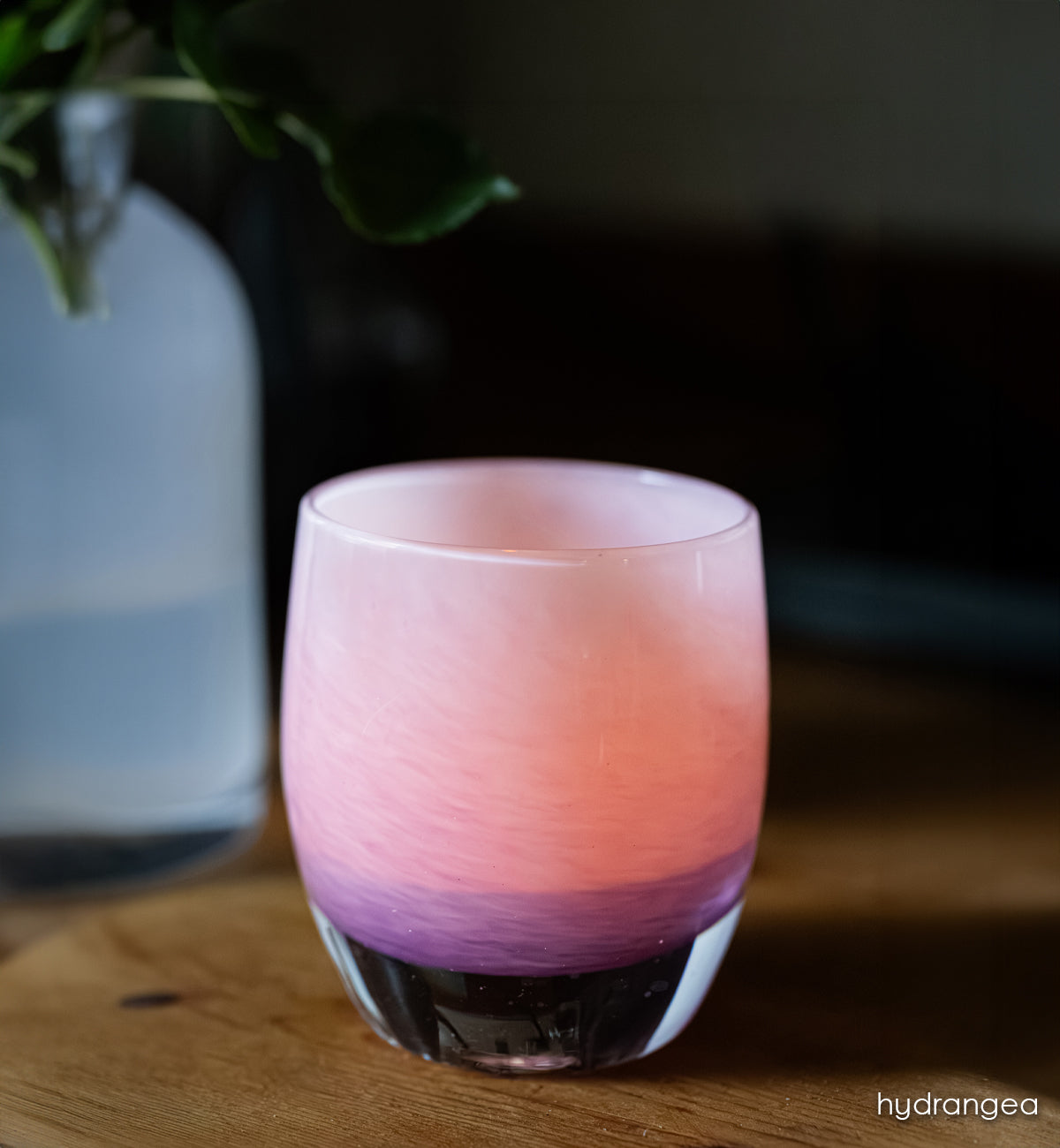 hydrangea | pink with purple ombré hand-blown glass candle holder on a wooden surface with a blurred background