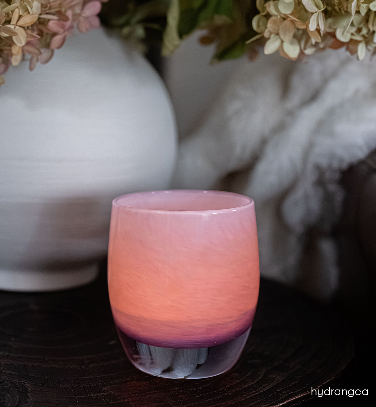 hydrangea | pink with purple ombré hand-blown glass candle holder on a dark surface with blurred decorative elements in the background