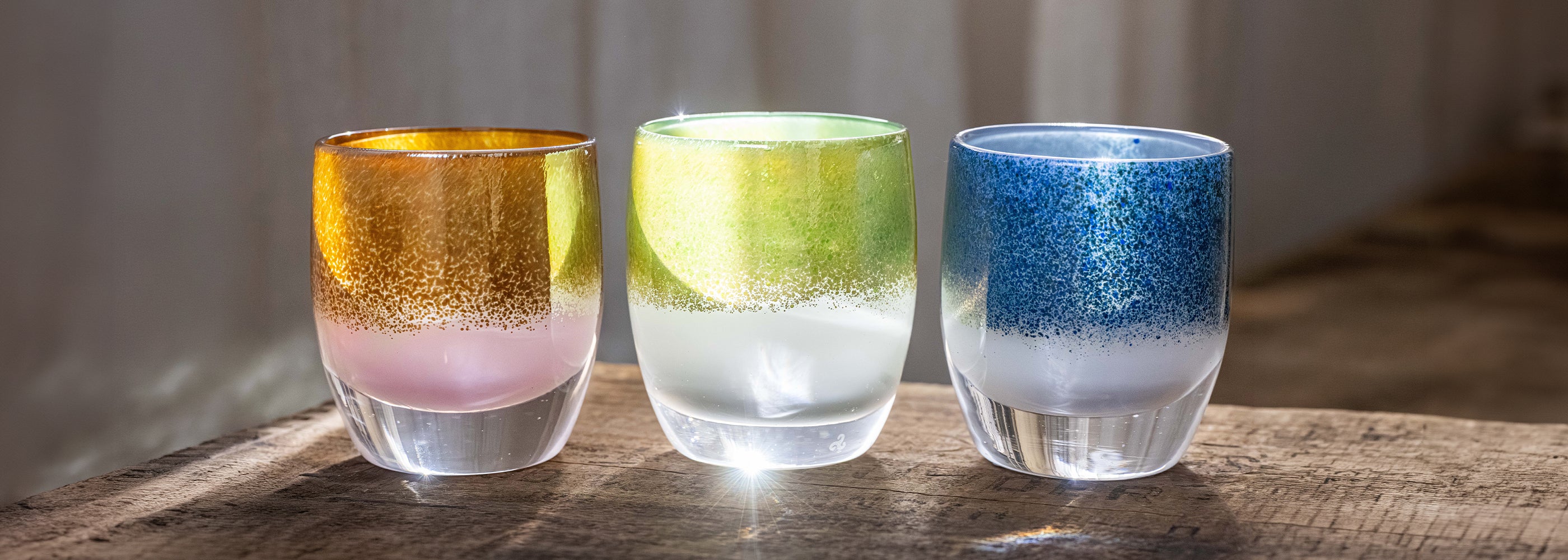 Three colorful glass candle holders on a wooden surface with a blurred background