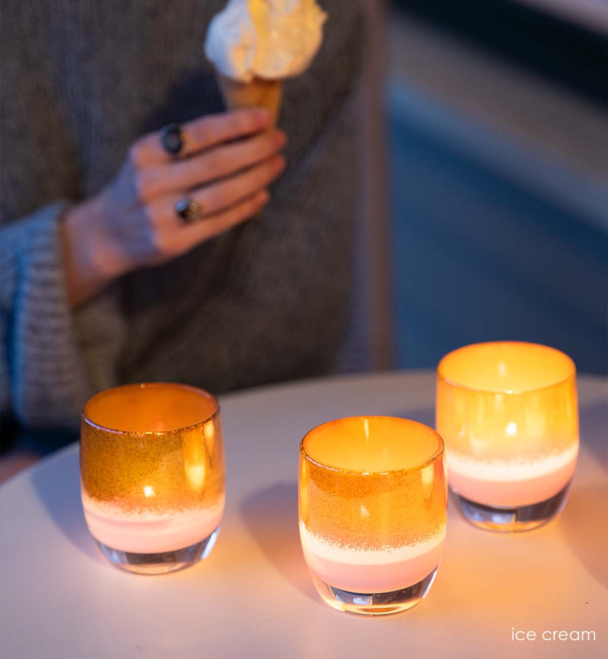 ice cream pink gold hand-blown glass votive candle holder lit on circular table with a person enjoying an ice cream cone in background.