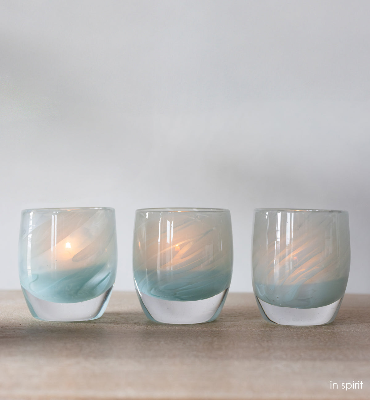 three 'in spirt' light blue hand-blown glass candle holder on wood shelf