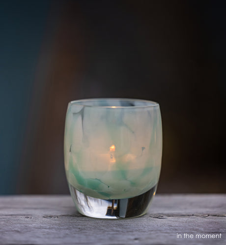 in the moment, blue, white, hand-blown glass votive candle holder with a lit candle on a wooden surface, dark background