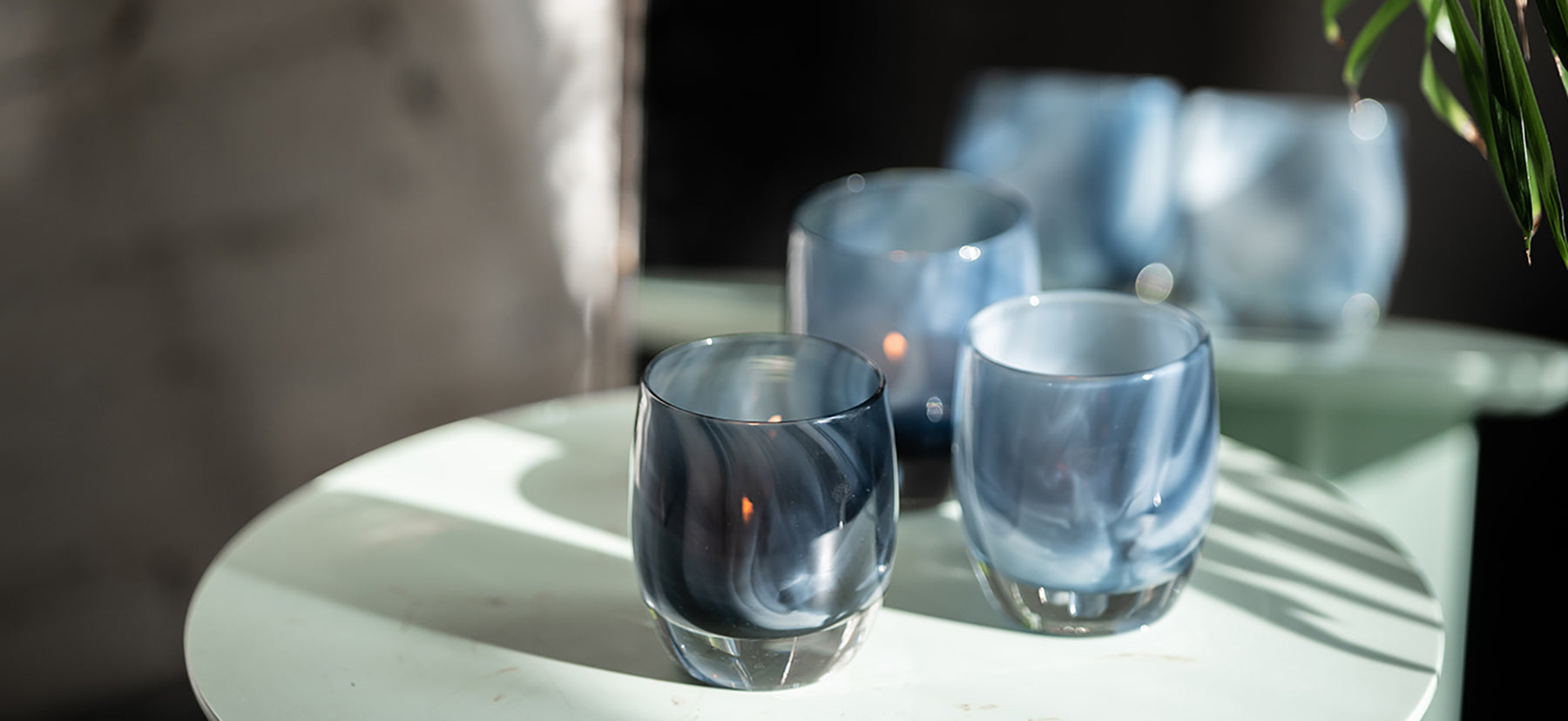 3 dark blue and white swirled patterned hand-blown glass candle holders names 'i see you' sitting on a white table in the sun.