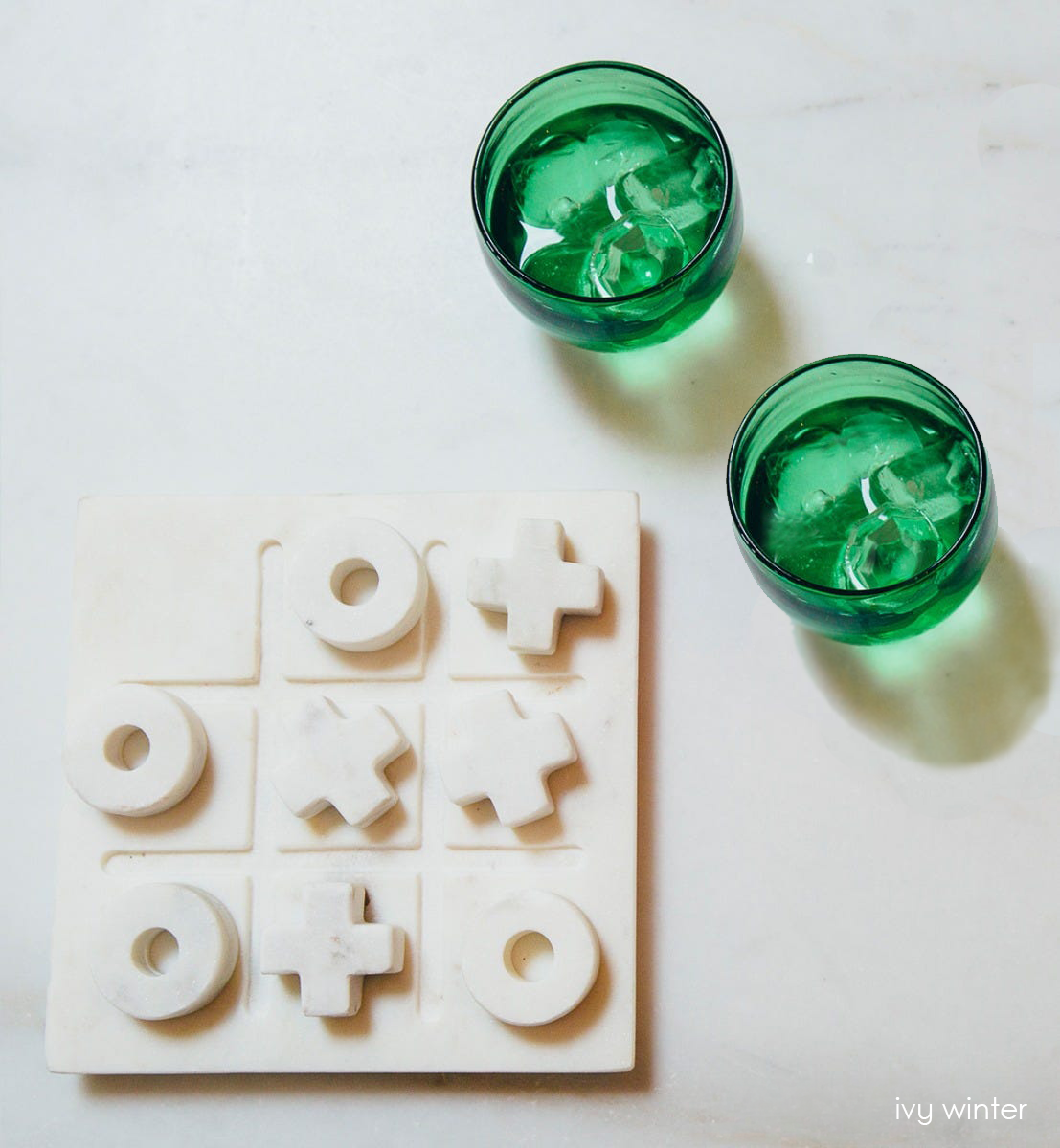ivy winter drinker set transparent green hand-blown drinking glass filled with ice and liquids next to a tic tac toe set.