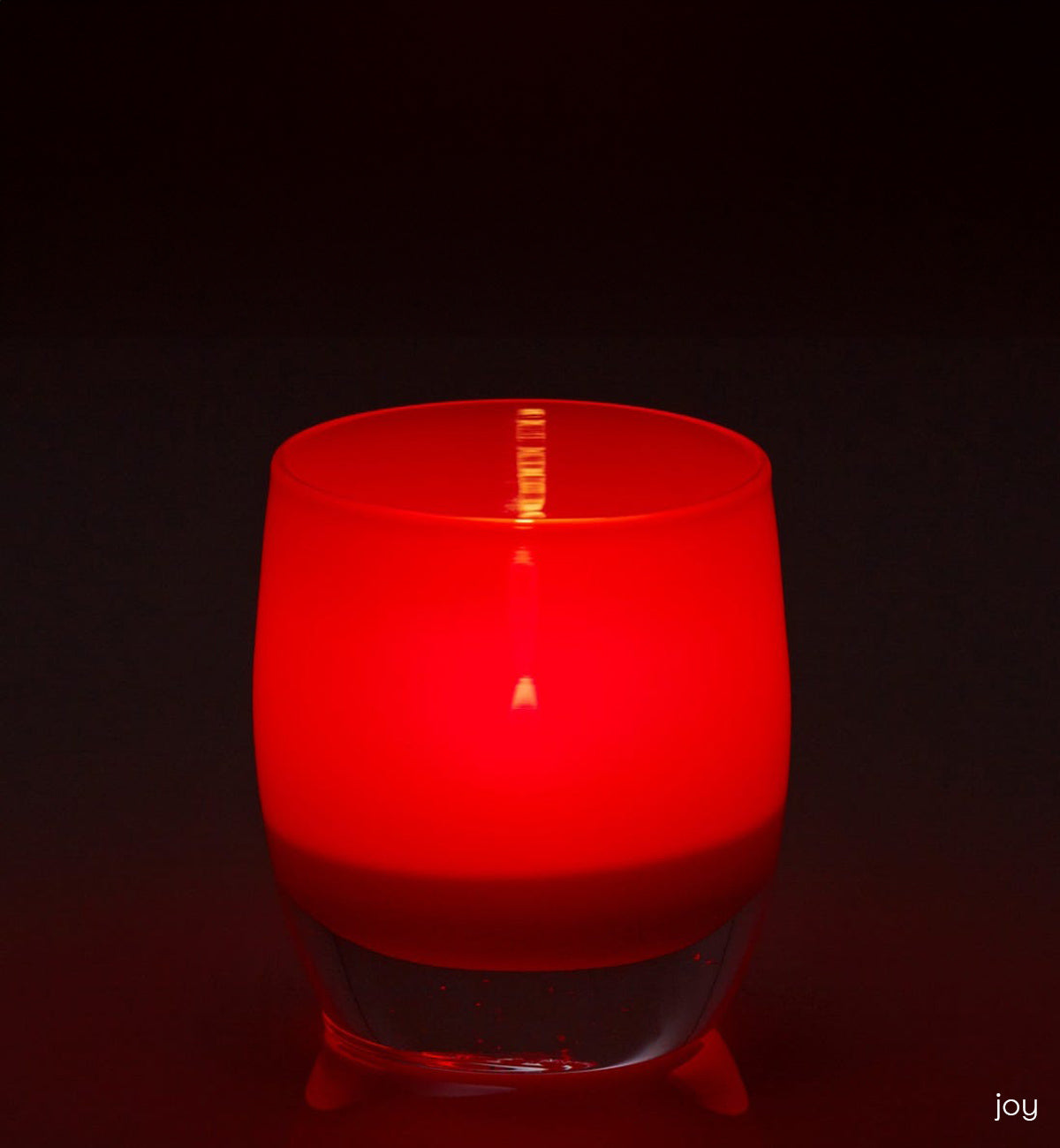 joy crimson red hand-blown glass votive candle holder on a reflective surface.