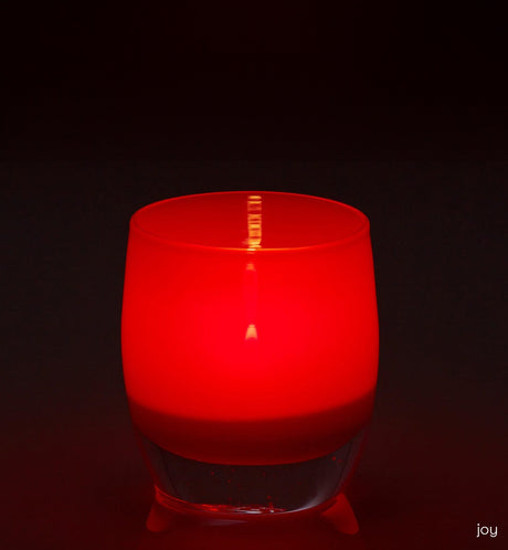 joy crimson red hand-blown glass votive candle holder on a reflective surface.