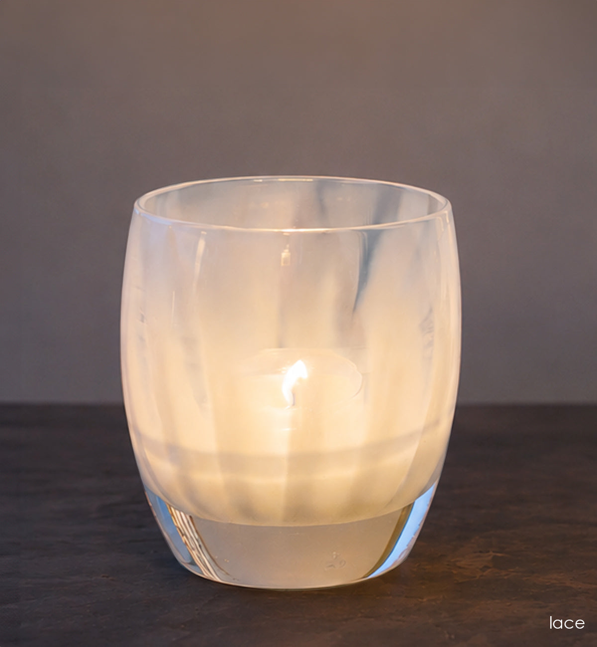 Frosted glass candle holder with a lit candle on a dark surface and gray background